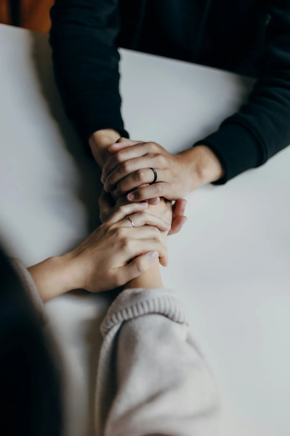 Dos personas sentadas frente a frente en una mesa, tomadas de las manos en señal de apoyo